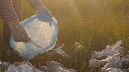 Environment, volunteer work to clean up the green planet, eco, collect garbage on green lawn in glare of the sunset, plastic waste bottles, glasses, protect hands from damage with protective gloves.