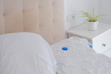 Full vacuum-sealed bag of duvets and pillows lying on bed next to big loose pile of unpacked bedding. Home organization, space-saving bedding storage