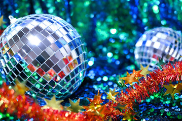 Christmas or New Year party celebration backdrop. Shiny silver disco balls and festive red tinsel with golden stars on a sparkling blue and green sequin background. Celebration concept.
