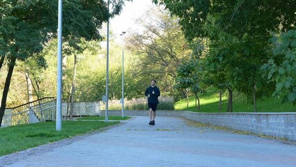 Young Caucasian man running in park on summer sunny day. Outdoor activities. Guy feeling pain after working out. Handsome man jogging outside. Sportsman is out of breath.