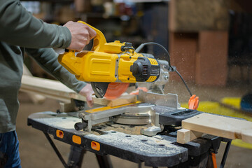 A professional carpenter saws the board with a circular saw. From under the disc of the circular saw, wood shavings, sawdust fly. Work in a furniture factory. High quality photo