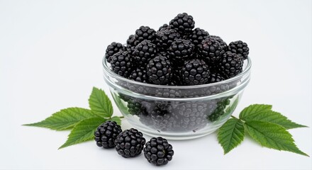 fresh blackberries in a glass bowl with green leaves on white background, healthy summer fruit