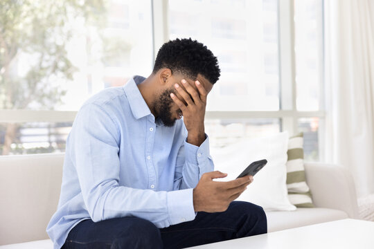 African man feels stressed sit on sofa with smartphone