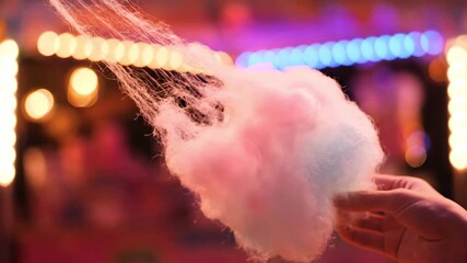 Cotton candy being held with colorful lights in the background  