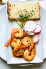 Seafood dish with shrimp, bread and radish slices. Seafood dish of cooked shrimp in sauce served with bread, butter and fresh radish slices on white background.