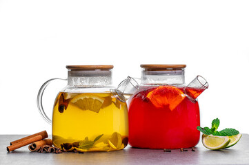 Two glass teapots with herbal and fruit tea. Two glass teapots with herbal yellow and red fruit teas served with citrus, mint and spices on white background.