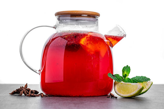 Red herbal tea with citrus and spices on table. Red herbal tea in glass teapot with citrus, cinnamon and cloves served with mint leaves on table close up. - Powered by Adobe