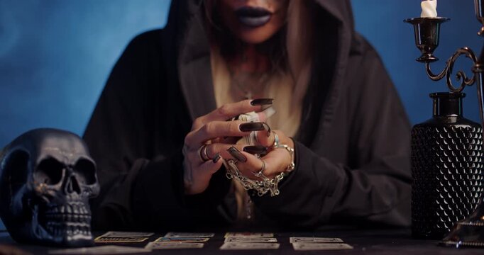 Witch shuffling tarot cards during mystical ritual with blue smoke