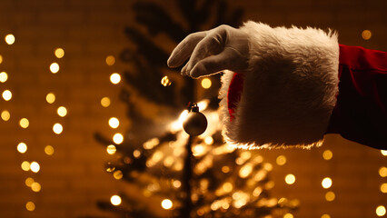 Santa gloved hand holds a glowing ornament against a background of festive lights and holiday cheer.