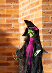 Hanging decorative green witch against a brick wall. Halloween celebration item. 
