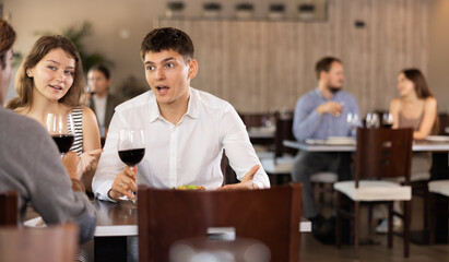 Couple young man and woman with adult man eat drink wine and chat in restaurant
