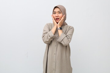 Young Asian woman in hijab is happy to hear gossip or very good news, looks at camera in amazement,...