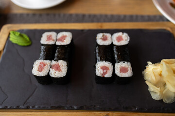 Sushi rolls are laid out on a black slate platter. Tuna rolls are served with wasabi and pickled ginger. Simple and elegant serving of the dish.