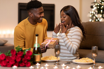A joyful moment occurs as a black boyfriend presents a wrapped gift to his surprised girlfriend.