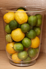Clear glass vase filled with fresh lemons and limes, showcasing vibrant citrus fruits against a warm wooden background.