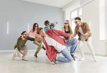 Plexiglas schilderij Dansschool Group of young funny hipsters girls and guys dressed in modern clothes, wearing sunglasses, dancing together in modern dance school studio, spacious room. Youth culture, style and hobby concept  © Studio Romantic