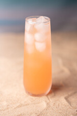 refreshing peach-colored beverage in frosted glass with ice on sandy surface evoking summer beach vibes and tropical relaxation in warm tones, contrast, sparkling, moisture, gradient, blur, elegant
