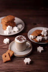 a cozy wooden table setup featuring a cup of frothy cappuccino topped with chocolate sprinkles accompanied by gingerbread cookies and star-shaped sugar pieces on elegant plates, delicious, sweet