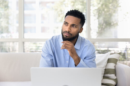 Pensive guy working on laptop looking away with thoughtful expression - Powered by Adobe