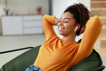 A young woman with curly hair smiles with her eyes closed, enjoying music through wireless earbuds....