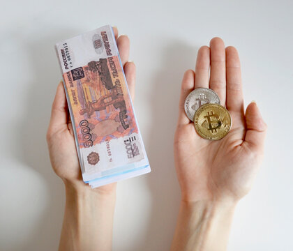 Two hands holding a Bitcoin coin and a stack of Russian rubles on a white background. Investing in cryptocurrencies. E-commerce, trading, mining, and blockchain. - Powered by Adobe