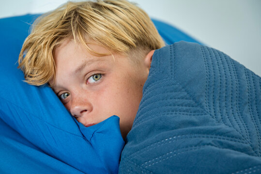 Young boy with open eyes lying awake in bed partially covered by blanket
