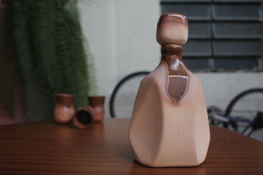 Botella de barro con tapa y un fondo desenfocado con vasos.
