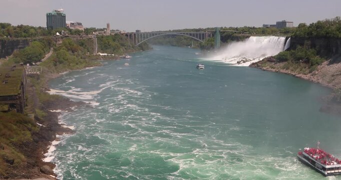 On the Niagara River, the Canadian tour boat with red ponchos is heading back from Horseshoe Falls, while the American blue-poncho boat moves in toward the mist below the border bridge.