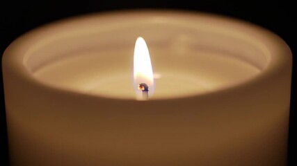 Close up of a lit candle with a bright flame casting light in a dark environment creating a warm glow