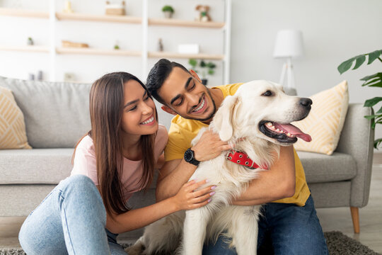 A young couple enjoys a playful moment with their golden retriever in a bright living room filled with plants and cozy decor. They share smiles and affection with their pet. - Powered by Adobe