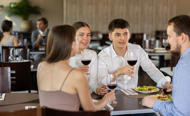 Two couples of young men and women drinking eating and talking in restaurant