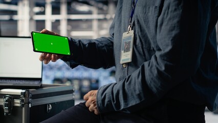 Obraz premium Data center worker uses isolated screen smartphone while deploying deep learning software. Server hub employee uses chroma key mobile phone while training AI systems with datasets, camera B