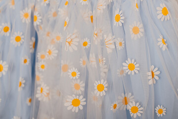 Blue tulle fabric with white daisy flower embroidery, delicate textile close-up.