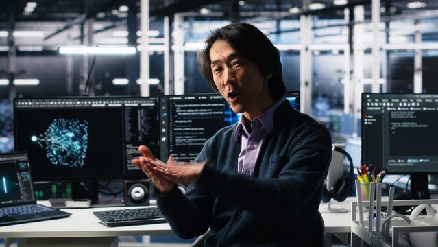 Data center admin waving hand, filming presentation tour, showcasing mainframes and AI technology. Upbeat Asian man in server room presenting artificial intelligence neural networks tech, camera A