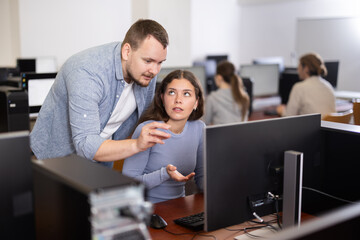 Male teacher of computer courses helps girl student to figure out with performance of difficult task, master ark. Mentor observes students studies, looks at monitor screen.