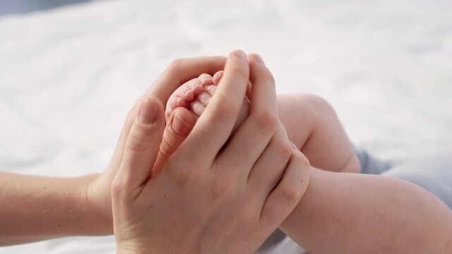 A loving interaction unfolds as a parent gently holds and caresses the tiny foot of their newborn baby while sitting on a soft bed in a cozy home environment filled with warmth and affection.