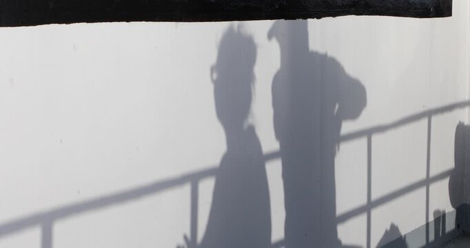 An intimate shadow of a couple cast on a white ferry wall, railing lines slicing through bright afternoon light. Minimal, anonymous and poetic&mdash;hinting at travel, closeness, and a quiet pause.