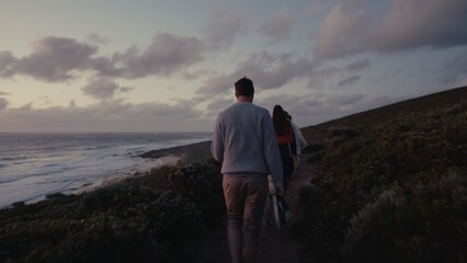 Couple walking along coastal trail at sunset near ocean waves