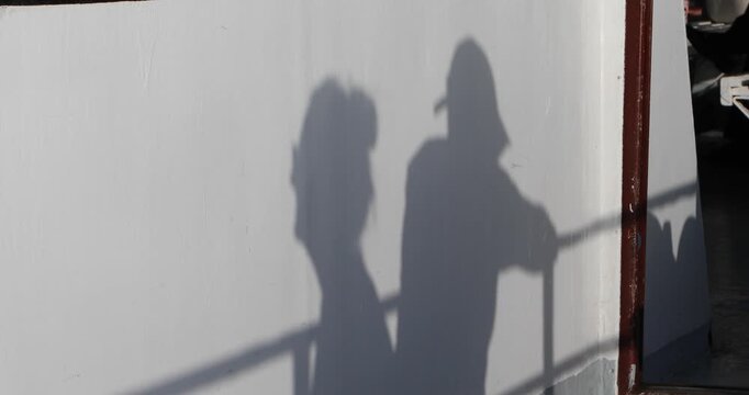 An intimate shadow of a couple cast on a white ferry wall, railing lines slicing through bright afternoon light. Minimal, anonymous and poetic&mdash;hinting at travel, closeness, and a quiet pause.