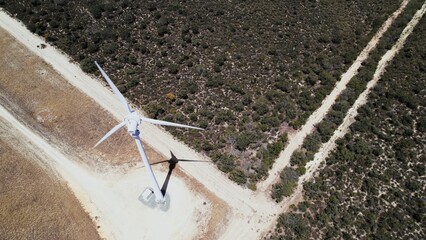 Wind turbine stands tall against a backdrop of rugged terrain and sparse vegetation during a clear day