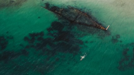 Exploring a shipwreck in clear turquoise waters near a rocky shoreline at sunset