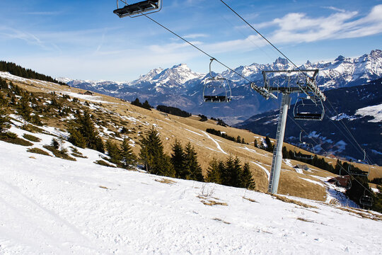 Chairlift above partially snow-covered slopes in Morzine Avoriaz ski resort, French Alps, during early spring with clear blue sky and mountain peaks in the distance.