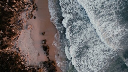 Waves crash on a sandy beach with rocky formations in the early morning light
