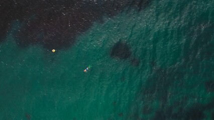 Two people swim in clear blue waters near a buoy during a sunny day at a coastal area