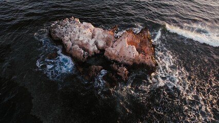 Rocky island surrounded by ocean waves at sunset captures the beauty of nature's coastal scenery