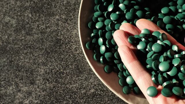 Spirulina algae tablets. Algae in nutrition.Hand pours spirulina tablets into a plate. Space for text. 4k footage