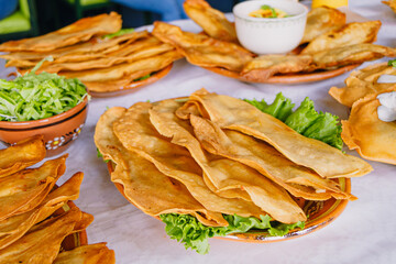 Abundant table featuring plates of molotes or fried quesadillas, served with shredded lettuce and cream, a classic Mexican street food.