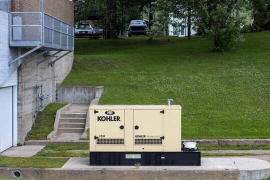 Canada, 24 July 2025 : Large industrial generator beside building, cars parked on grassy hill.