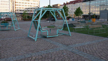 Public square with modern turquoise swings and benches in evening light