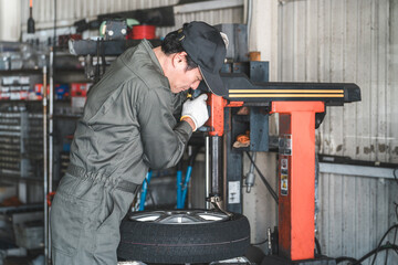 タイヤチェンジャーを使いタイヤの組み替えをするメカニック・整備士の男性作業員
